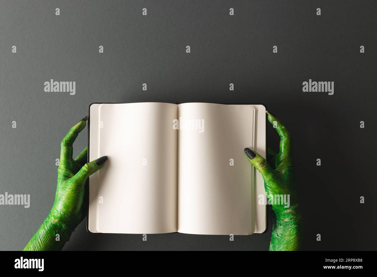 Lancette di mostri verdi che reggono il notebook con spazio per la copia su sfondo grigio Foto Stock