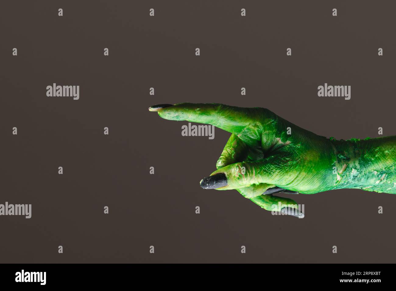 Mano mostro verde con unghie nere che puntano con il dito su sfondo grigio Foto Stock