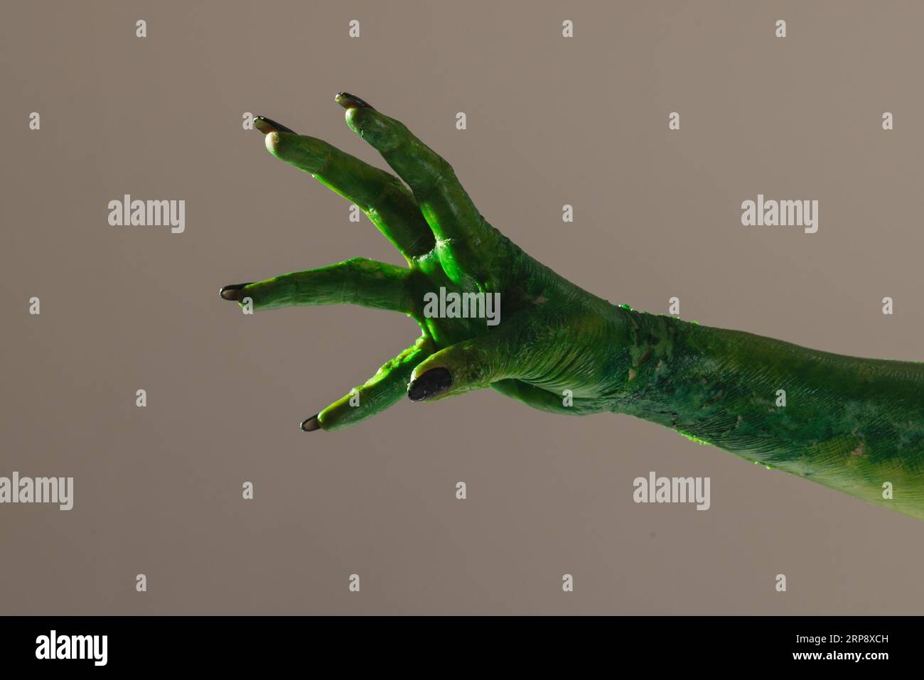 Mano mostro verde con unghie nere che raggiungono lo sfondo grigio Foto Stock