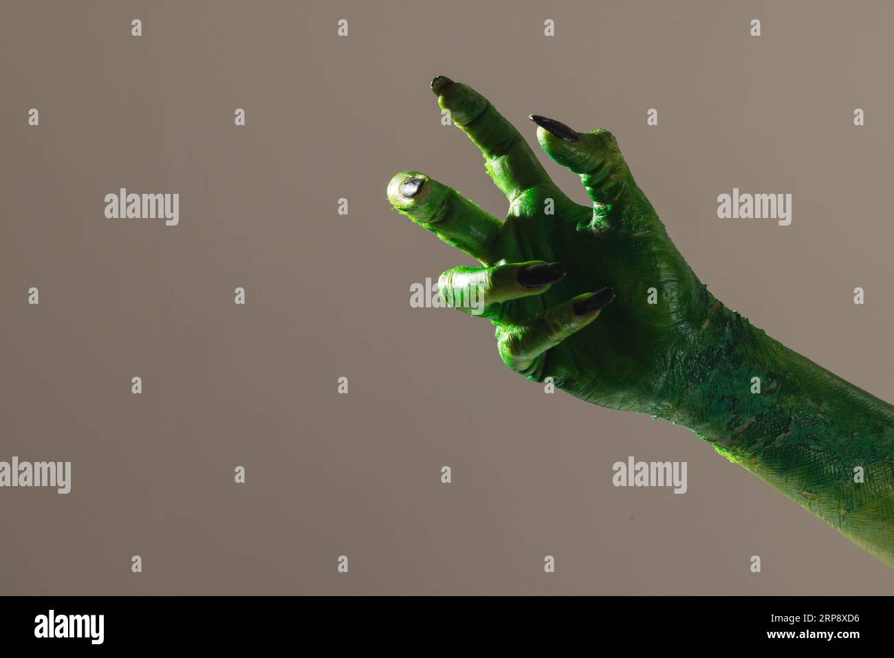 Mano mostro verde con unghie nere che fanno gesto su sfondo grigio Foto Stock