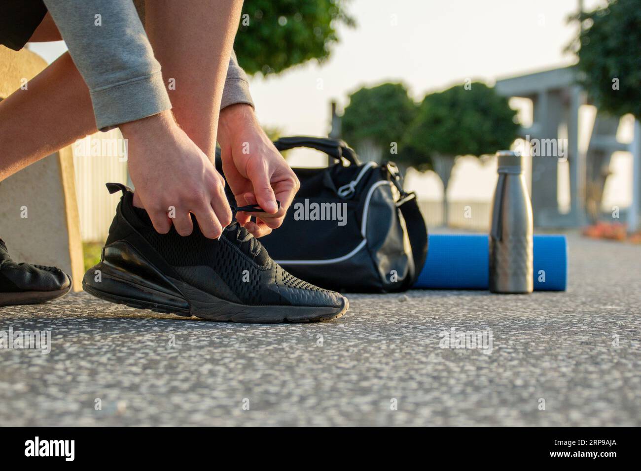 Primo piano delle mani di un giovane uomo che si lega alle sneakers. Borsa sportiva, tappetino e bottiglia d'acqua sullo sfondo Foto Stock
