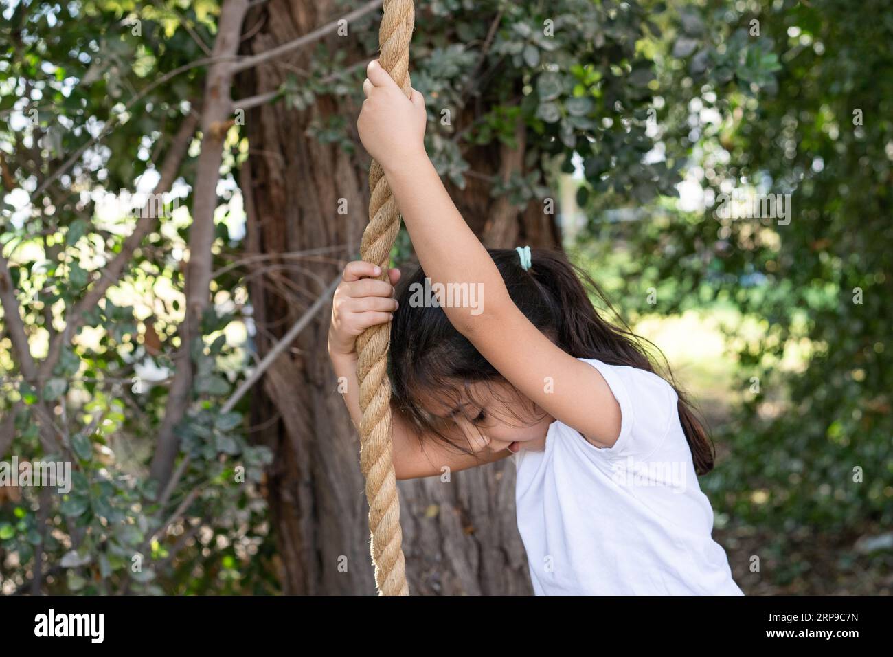 Esplorazione del cortile. Little Girl arrampicata sulla corda, abbracciando il parco giochi della natura per avventure coraggiose. Foto Stock