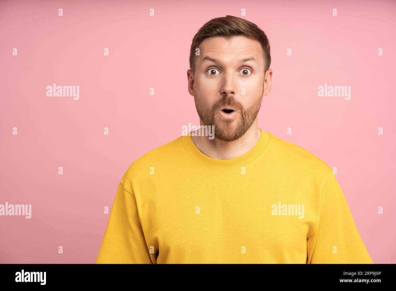 Un uomo stupito che guarda a bocca aperta sorprende l'espressione con gli occhi grandi e lo sfondo rosa isolato dello studio. Foto Stock