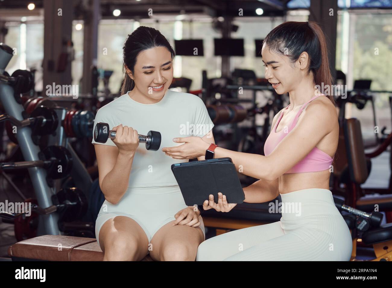 Giovane donna e un personal trainer con allenamento pesi manubri in palestra. Foto Stock