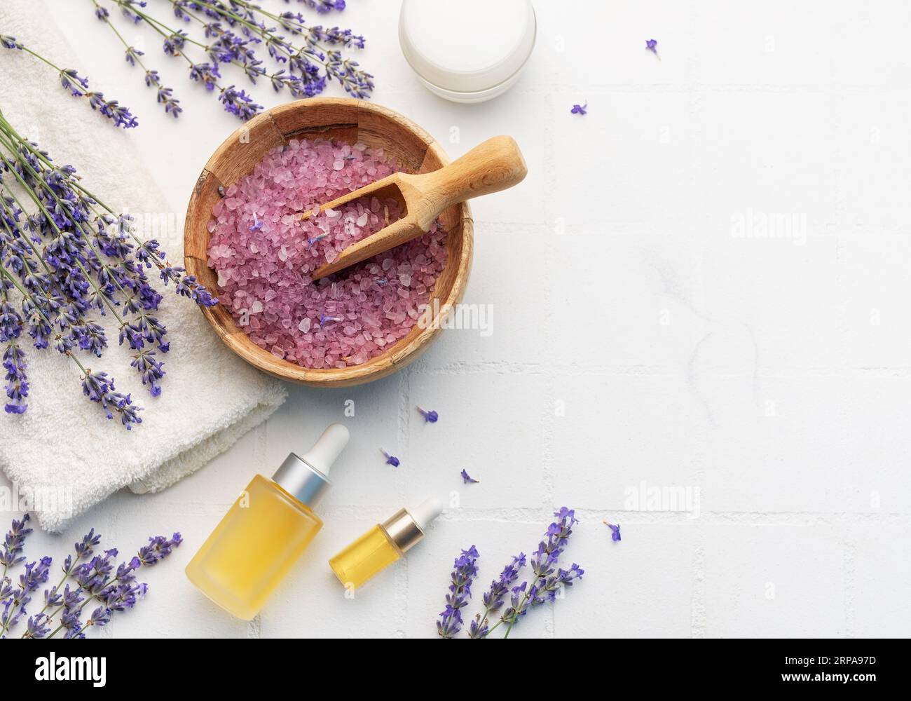 Vasca idromassaggio con lavanda. Sale di lavanda, olio essenziale naturale e lavanda fresca su fondo di piastrelle bianche. Foto Stock
