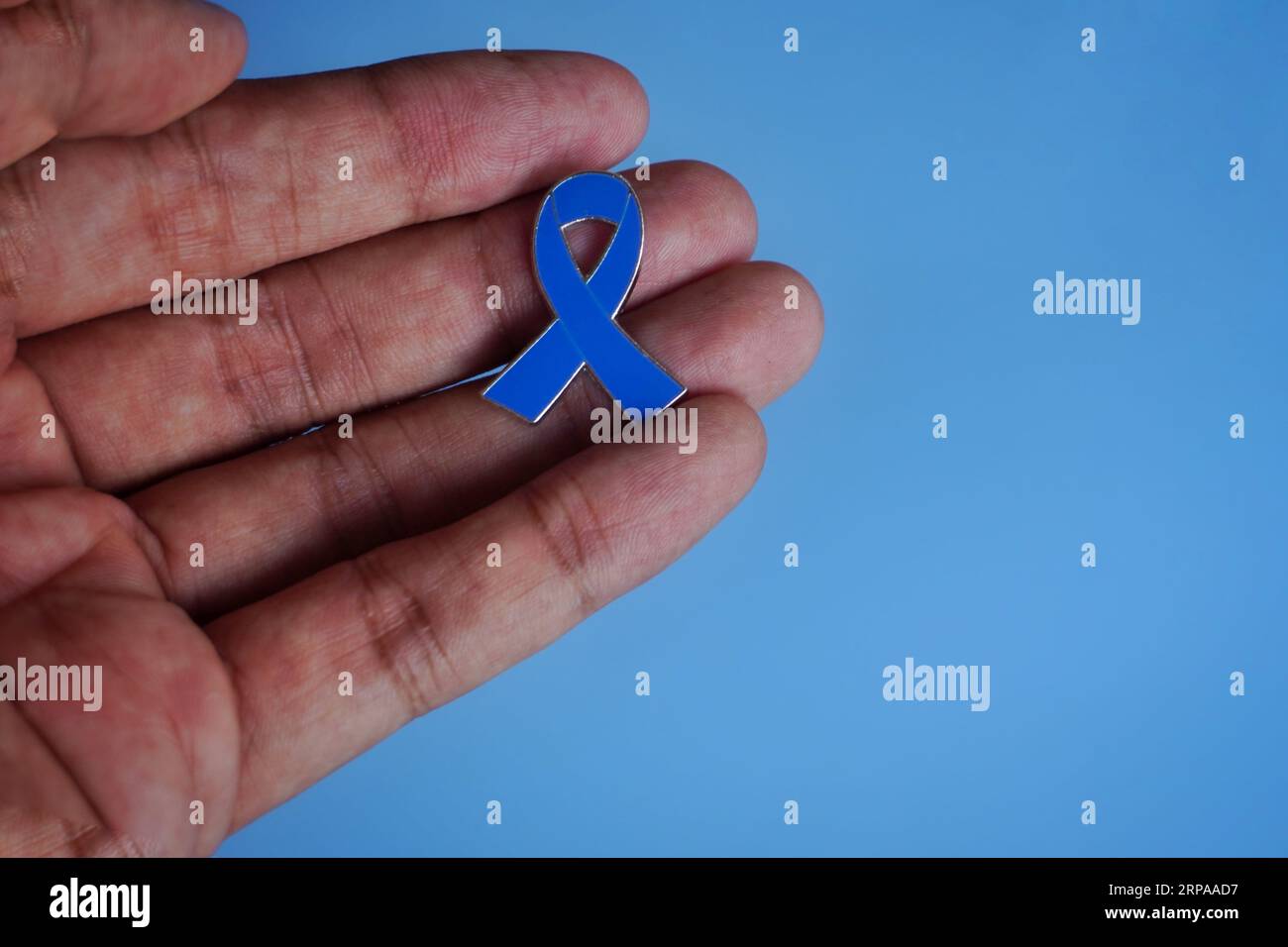 Mano che tiene il nastro blu su sfondo blu con spazio per la copia. Concetto di consapevolezza del cancro Foto Stock