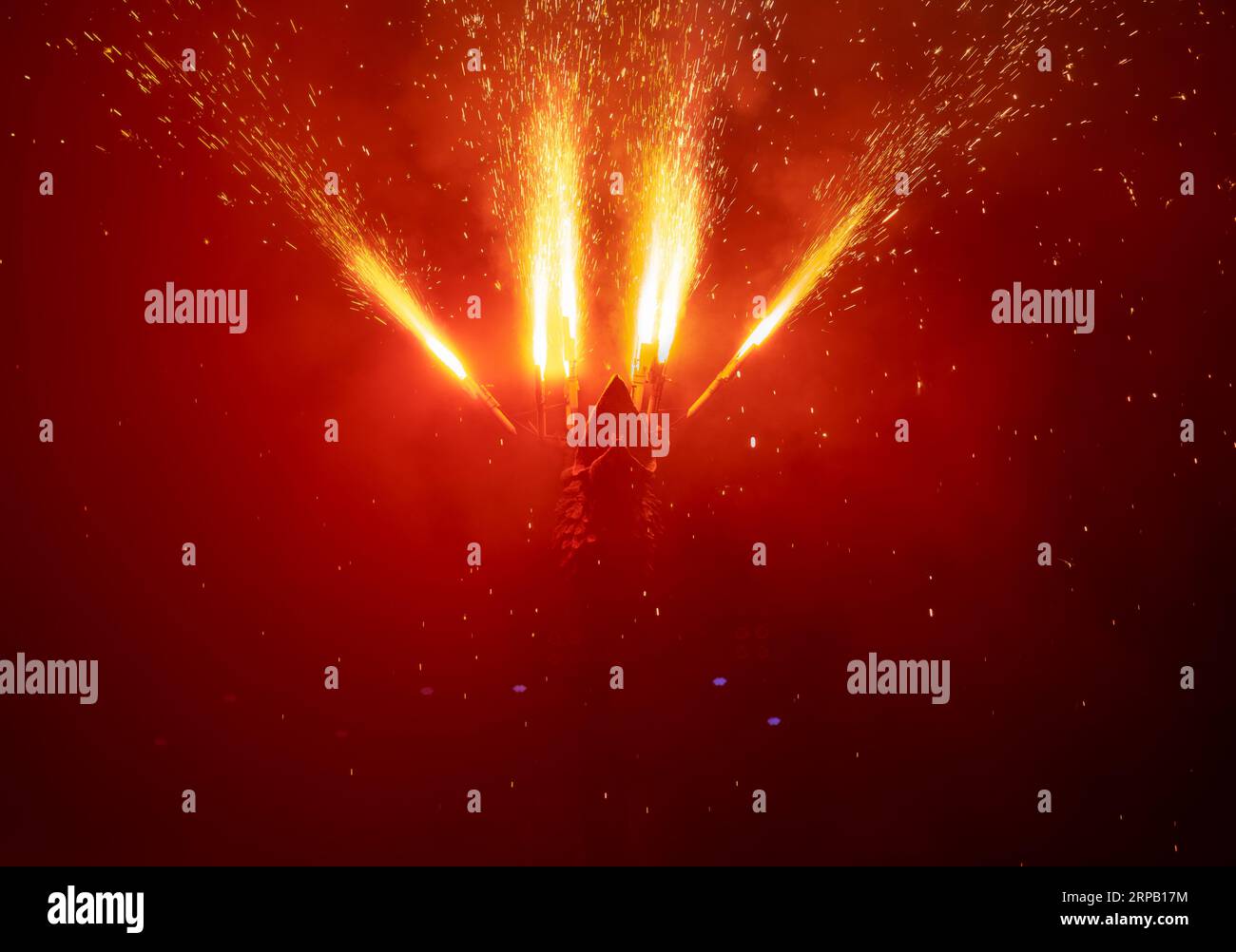 Testa di drago che guarda verso l'alto, espellendo fuochi d'artificio dalle ali e creando una pioggia di scintille di fuoco che cadono e illuminano in modo poco chiaro l'oscurità del Foto Stock