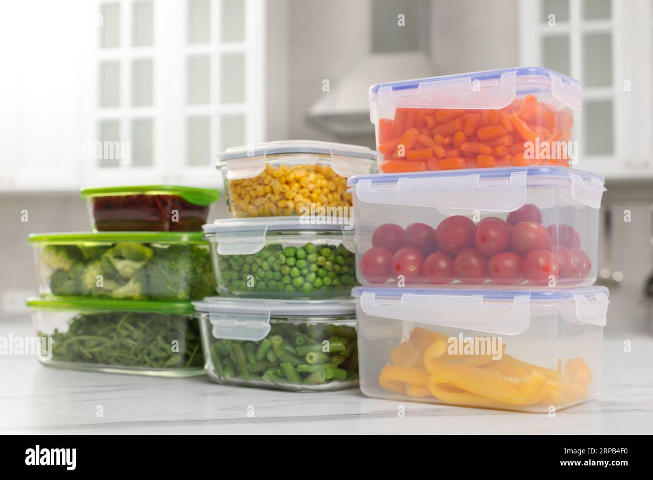 Contenitori in vetro e plastica con diversi prodotti freschi su un tavolo in marmo bianco in cucina. Conservazione degli alimenti Foto Stock