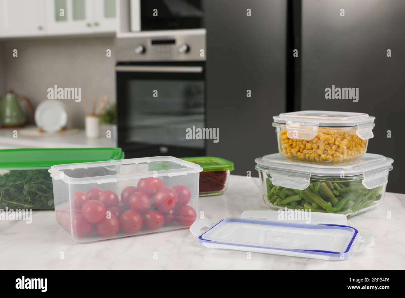 Contenitori in plastica e vetro con diversi prodotti freschi su tavolo in marmo bianco in cucina, spazio per testo. Conservazione degli alimenti Foto Stock