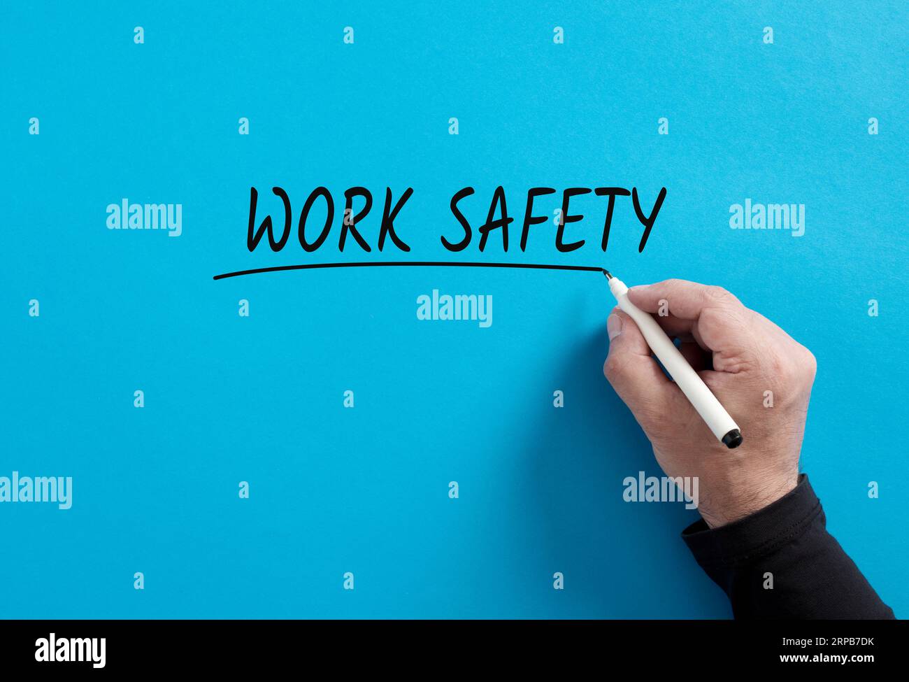 Mano maschile sottolinea la parola sicurezza sul lavoro su sfondo blu. Proteggere i lavoratori dai pericoli sul lavoro. Sicurezza sul luogo di lavoro. Foto Stock