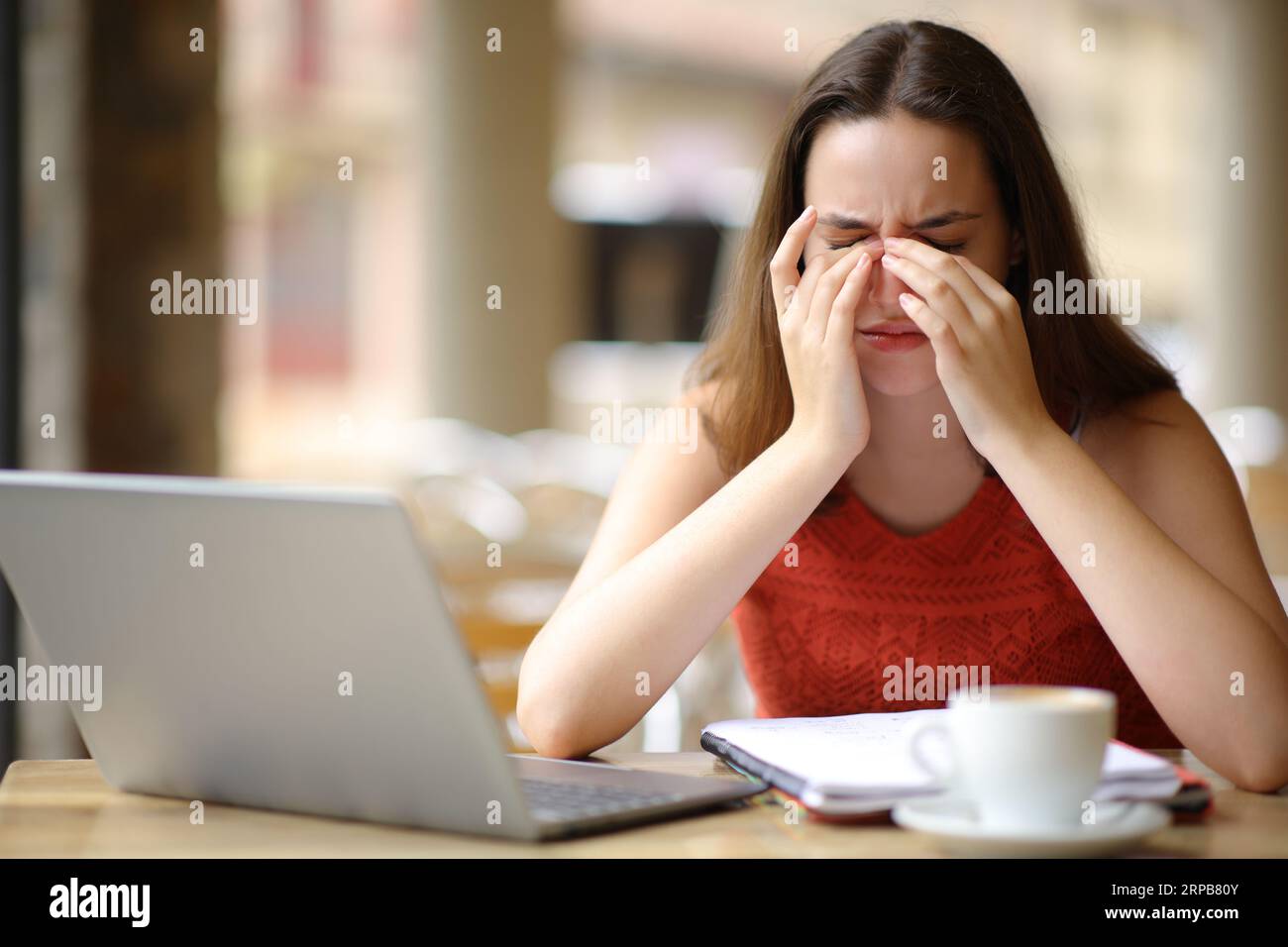 Ritratto frontale di uno studente affetto da affaticamento oculare dopo aver utilizzato un computer portatile in una terrazza bar Foto Stock