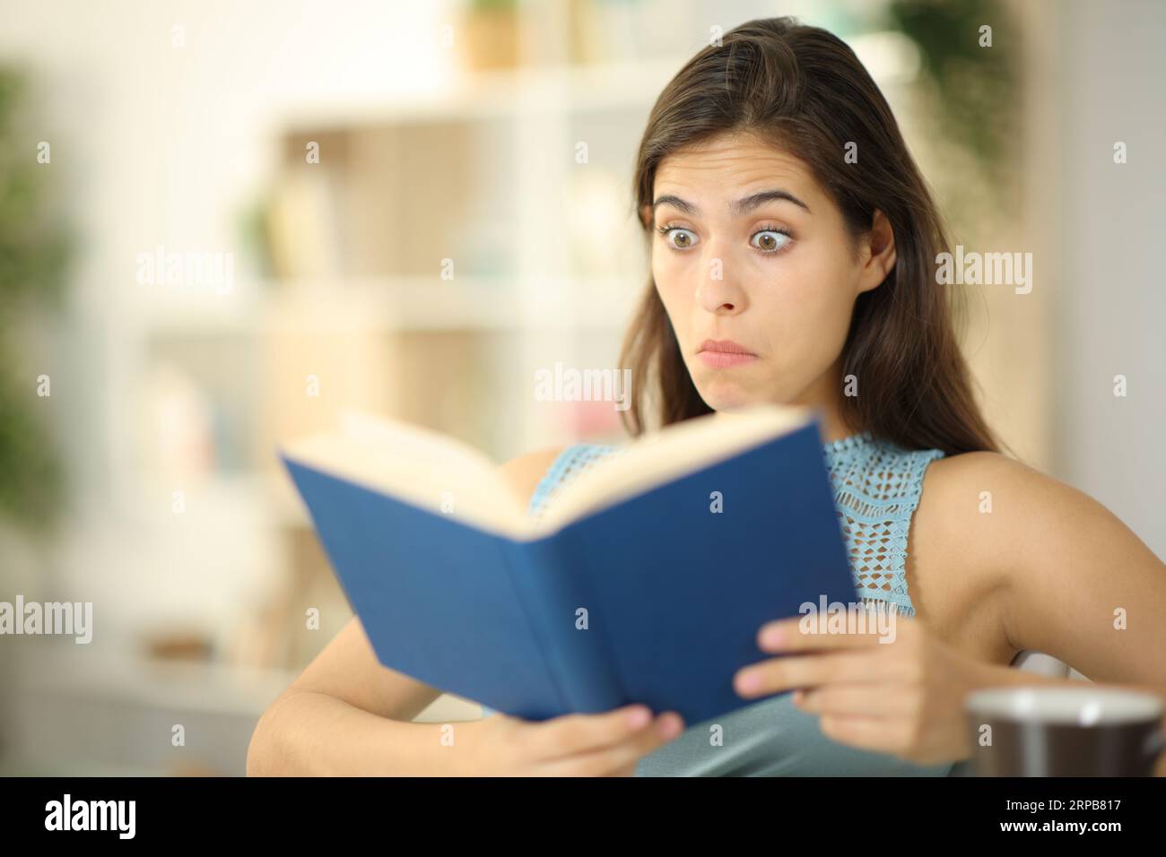 Lettore di libri perplesso che legge seduto a casa Foto Stock
