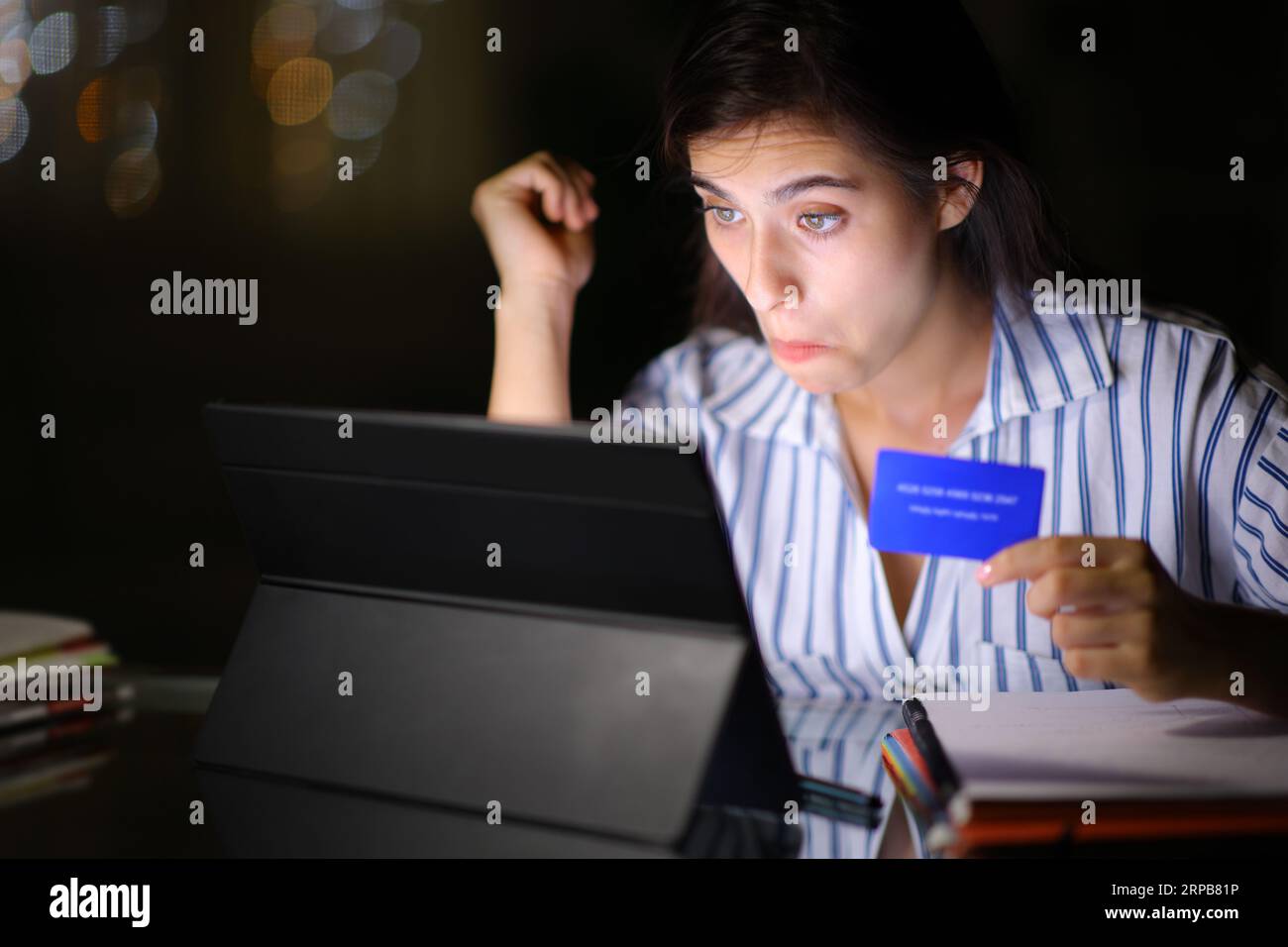 Studente perplesso che acquista online con carta di credito e laptop di notte a casa o in ufficio Foto Stock