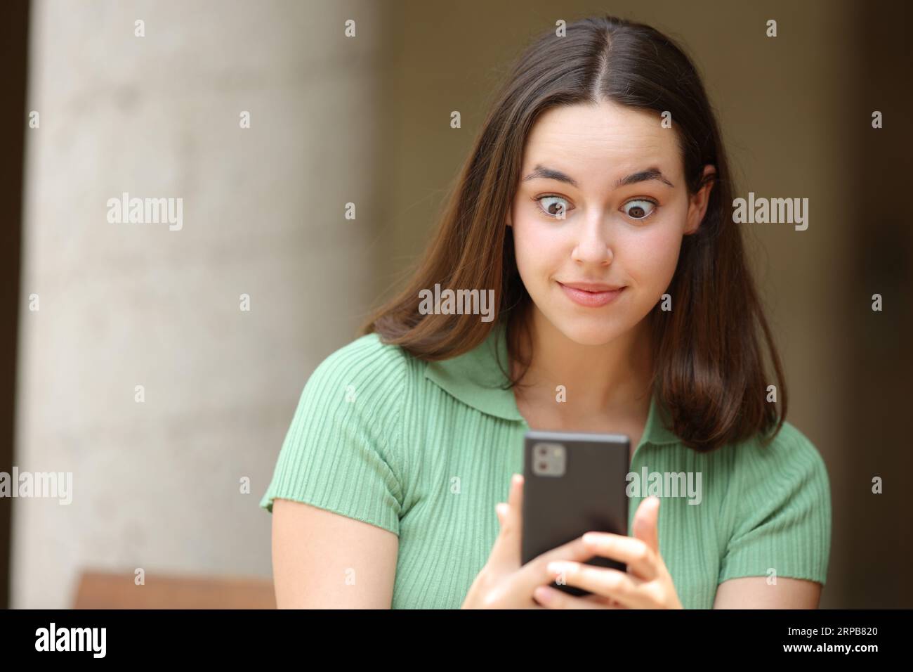 Ritratto frontale di una donna scioccata che controlla il cellulare per strada Foto Stock