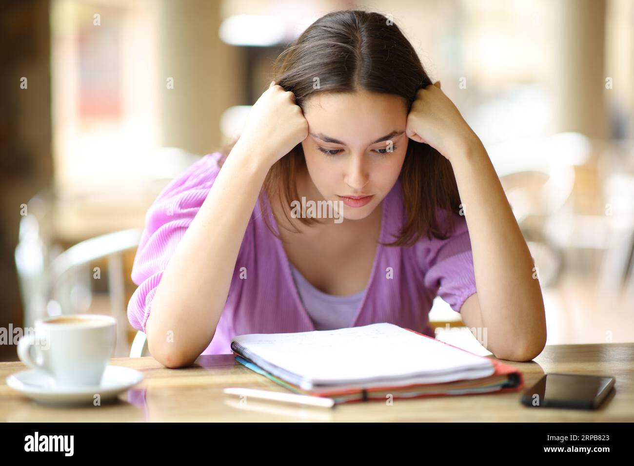 Studente che studia appunti difficili da leggere da un notebook in una terrazza del ristorante Foto Stock