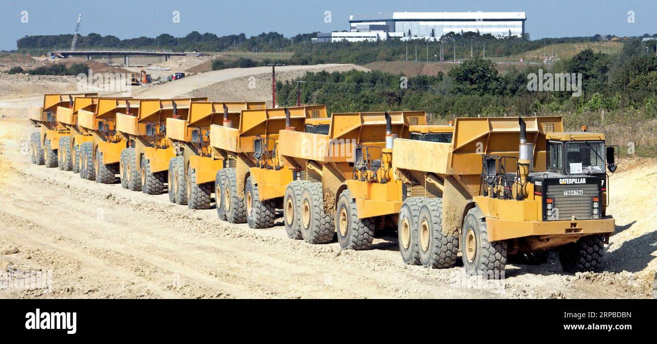 Lunga serie di sette dumper Caterpillar su un nuovo cantiere autostradale per formare la strada di collegamento con l'aeroporto di Stansted, vicino a Takeley, nell'Essex, Inghilterra, Regno Unito Foto Stock