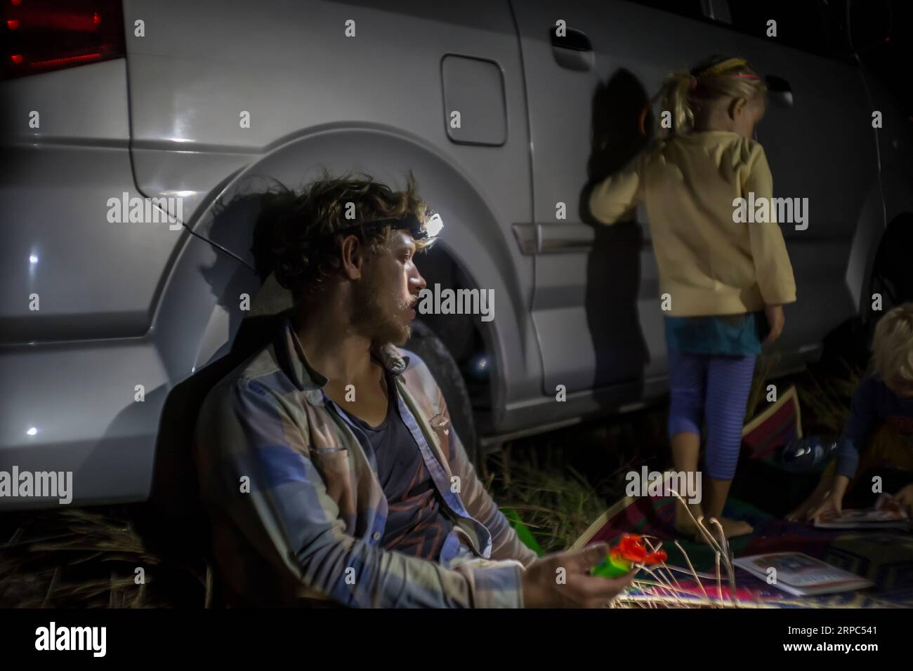 Uomo con faro seduto contro furgone di notte Foto Stock