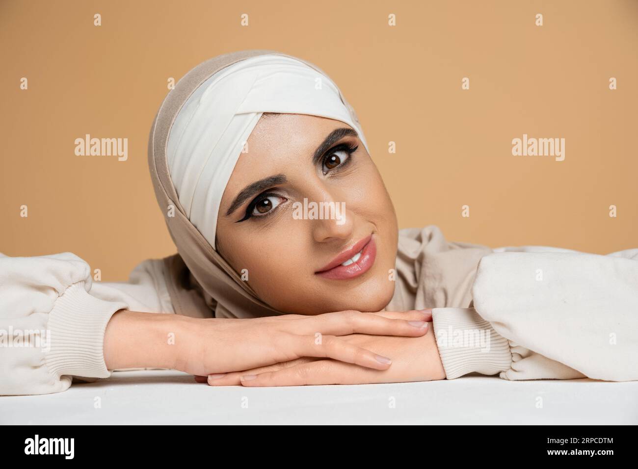 ritratto della donna mediorientale in hijab, con trucco che guarda la macchina fotografica su beige, bellezza musulmana Foto Stock