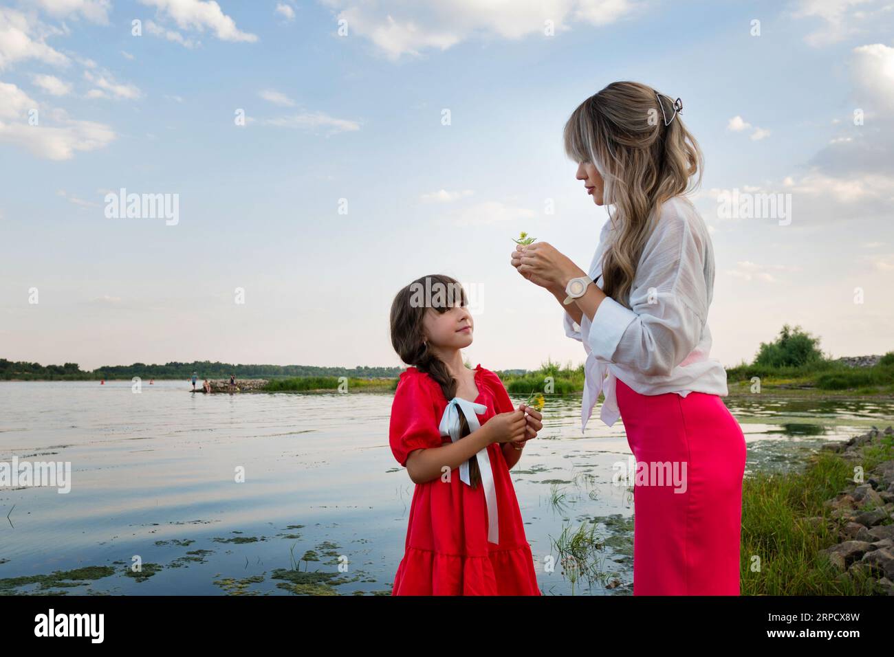 Mamma e figlia stanno camminando vicino al lago. Una famiglia felice passa del tempo insieme. Madre e ragazza che si divertono vicino allo stagno Foto Stock