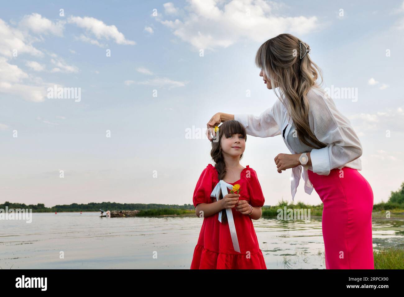 Mamma e figlia stanno camminando vicino al lago o allo stagno. Madre che fissa i capelli della bambina Foto Stock