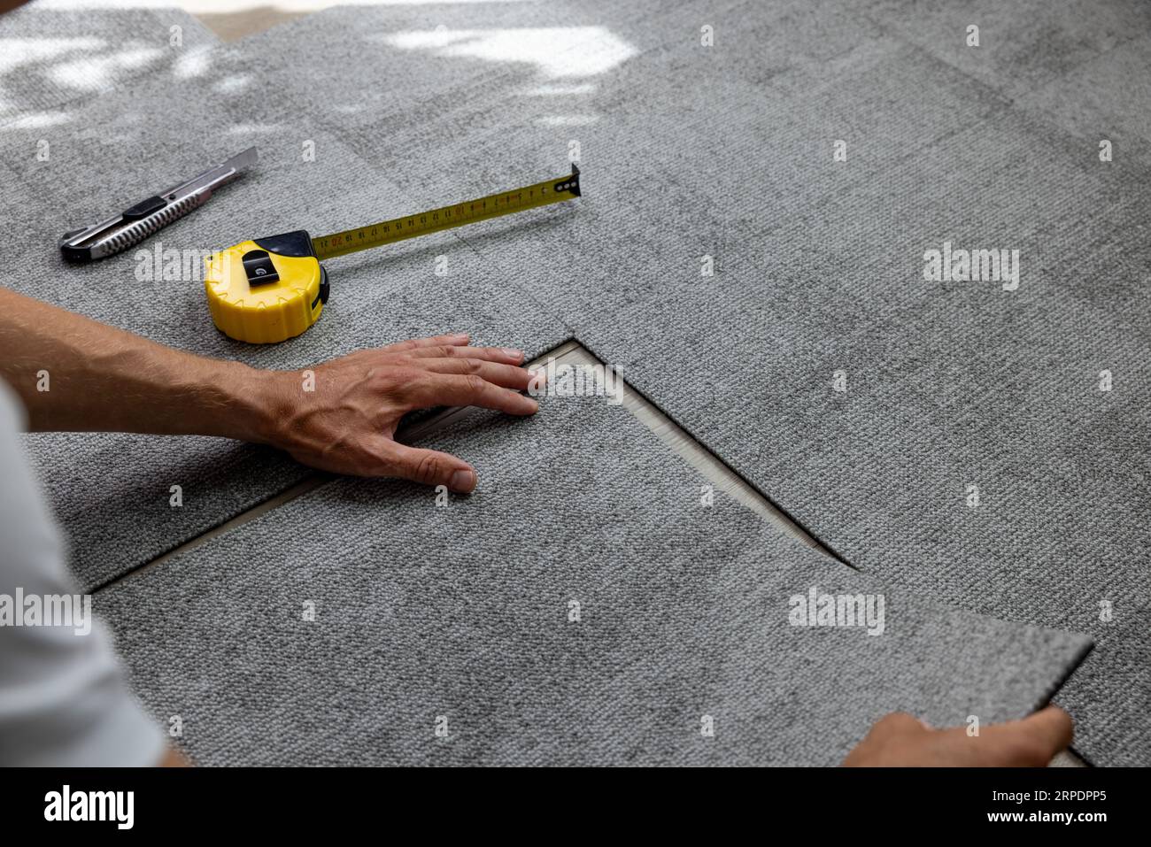 lavoratore che installa le piastrelle per moquette sul pavimento Foto Stock