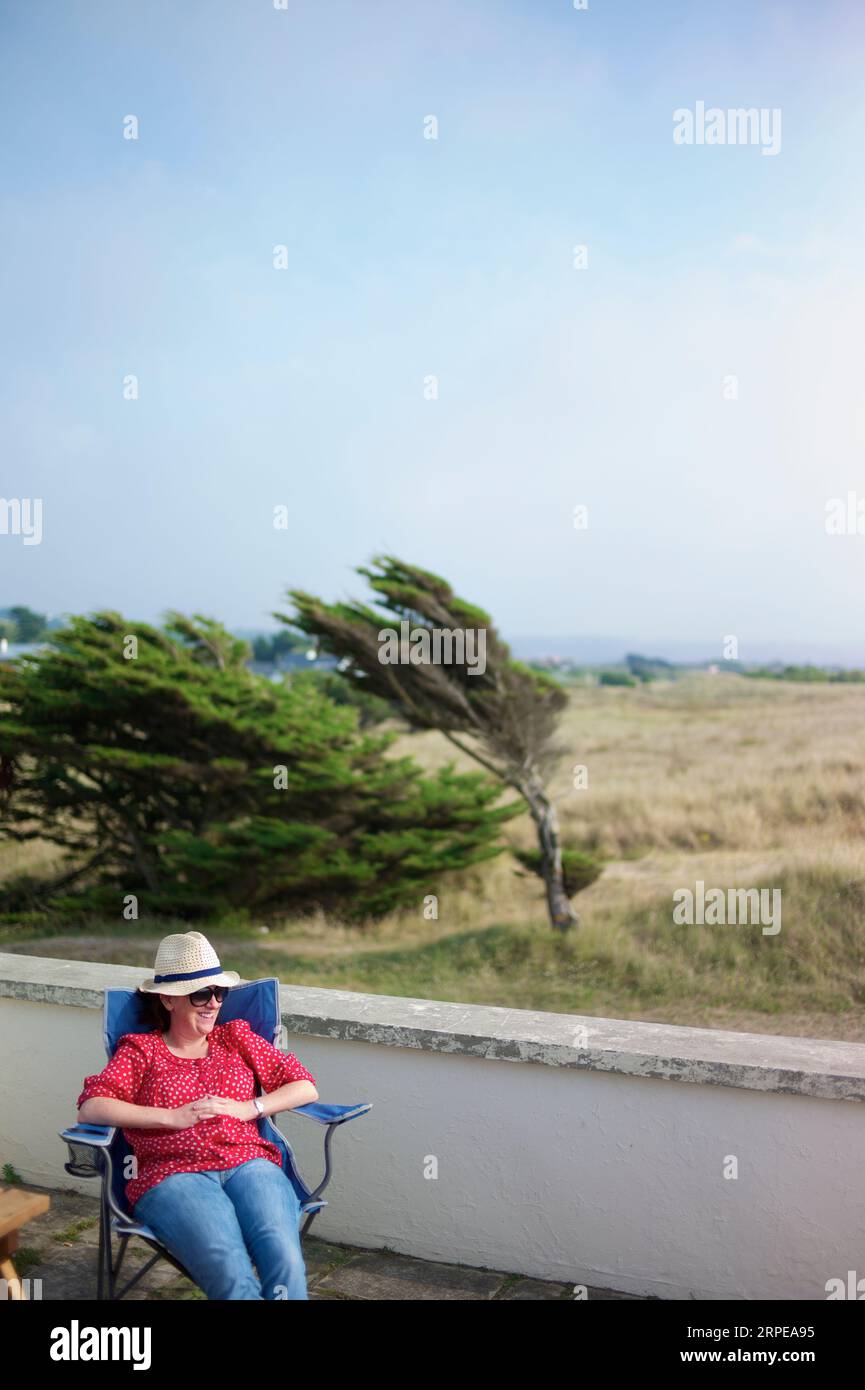 La giovane donna che indossa una camicia rossa e indossa un cappello bianco gode del sole estivo. Foto Stock