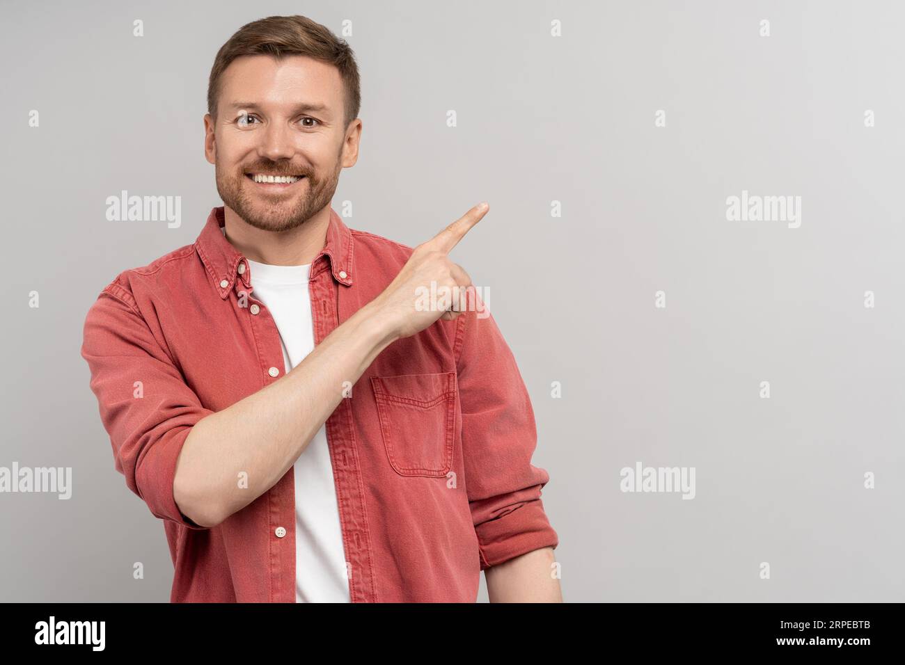Amity uomo sorridente che punta il dito indice a fianco sullo spazio di copia per la pubblicità sullo sfondo dello studio. Foto Stock
