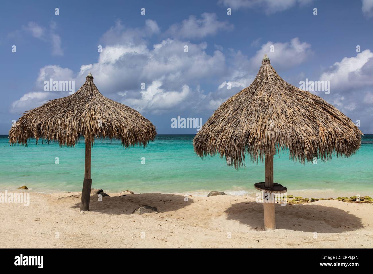 Ombrelloni di bambù sulla spiaggia sabbiosa dell'isola di Aruba. Acque turchesi al largo; nuvoloso cielo blu dietro. Foto Stock