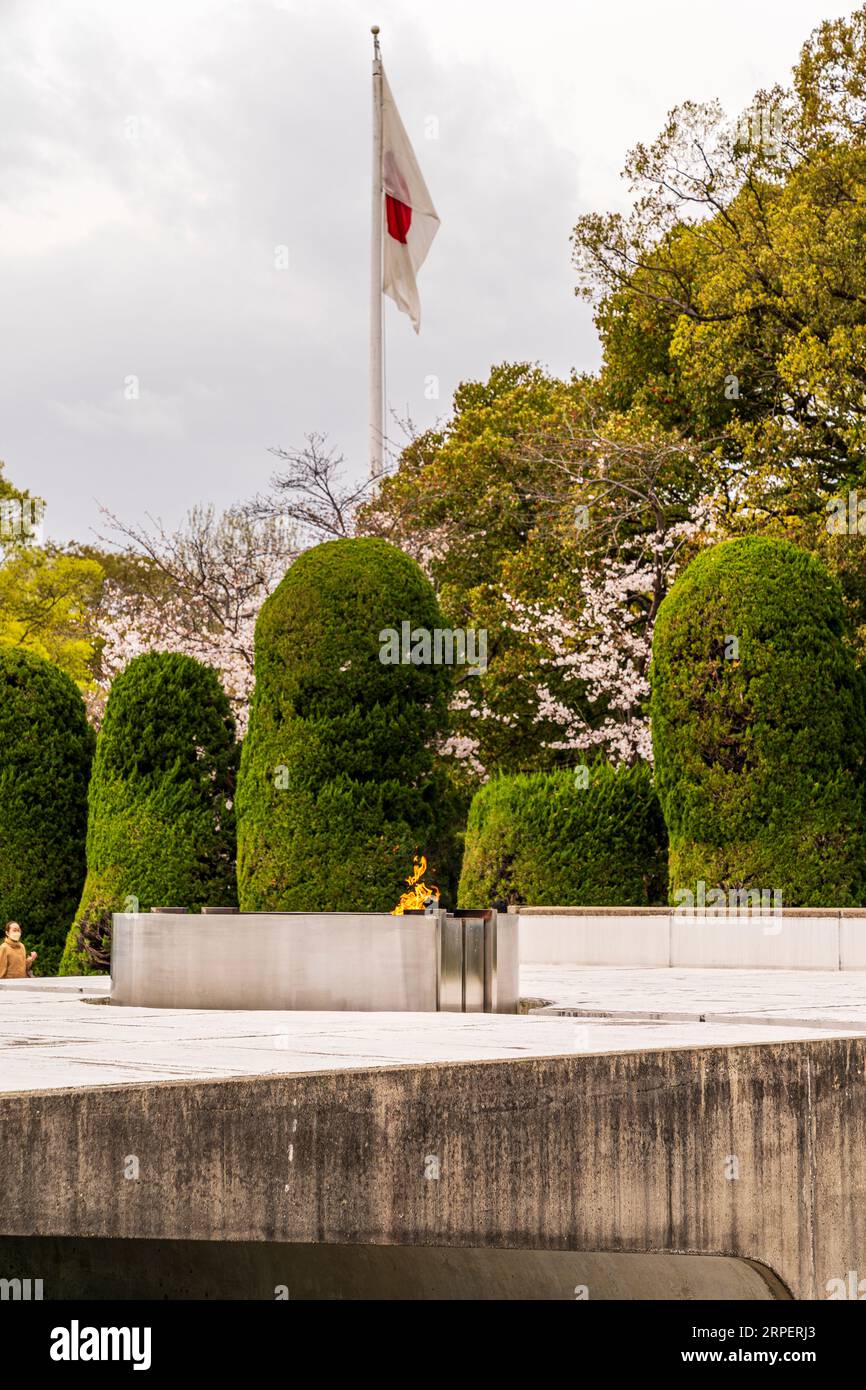 La fiamma della Pace, progettata da Kenzo Tange, presso il parco Memoriale della Pace di Hiroshima con la bandiera giapponese appesa sullo sfondo. Foto Stock