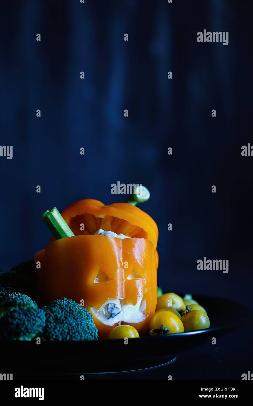 Colorato peperone dolce arancio ripieno come mostro con il volto tagliato in una zucca di Halloween Jack o'Lantern e riempito con Tzatziki DIP. Se Foto Stock