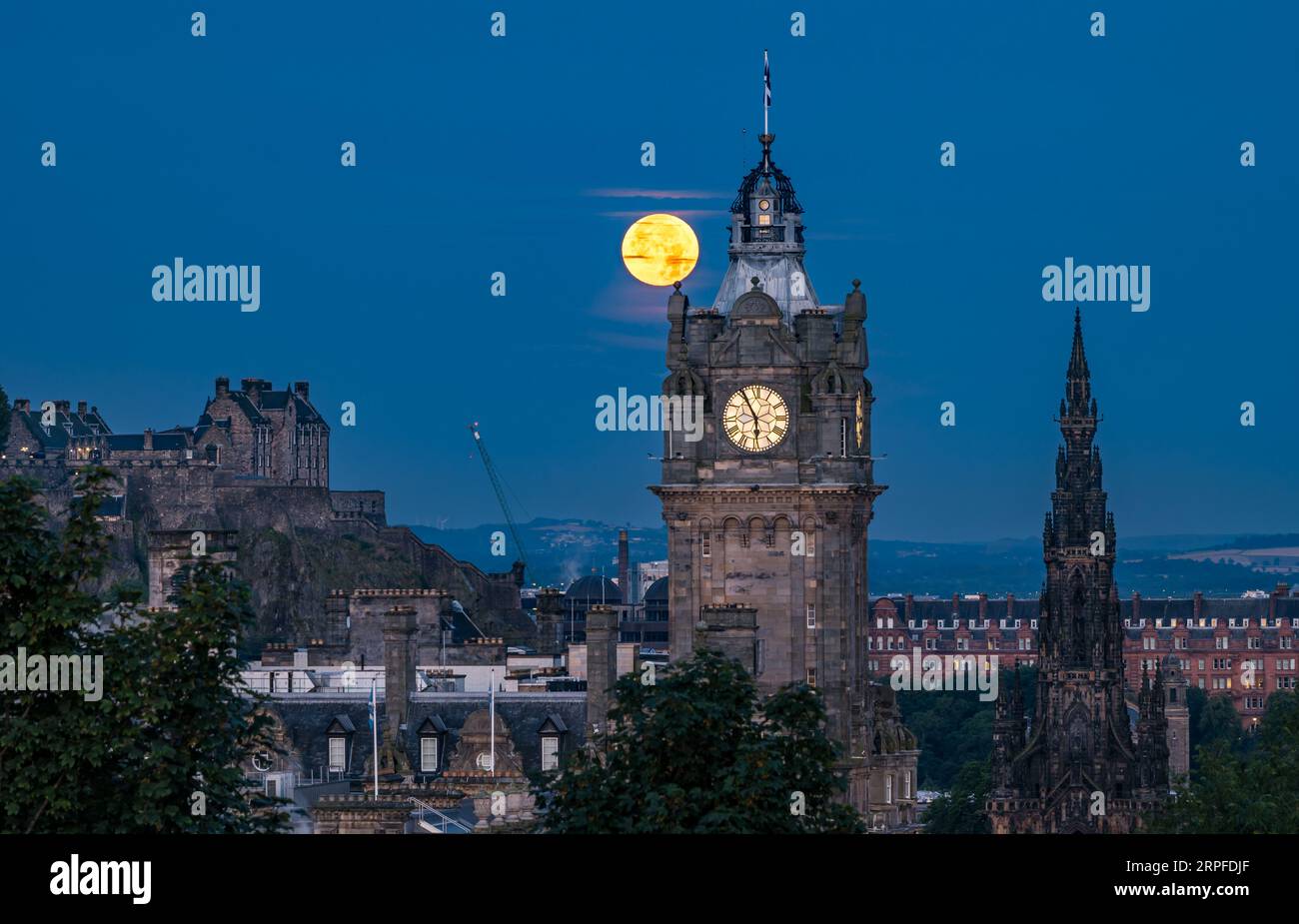 Skyline della città con una superluna blu sulla torre dell'orologio Balmoral, monumento Scott e castello di Edimburgo, Scozia, Regno Unito Foto Stock