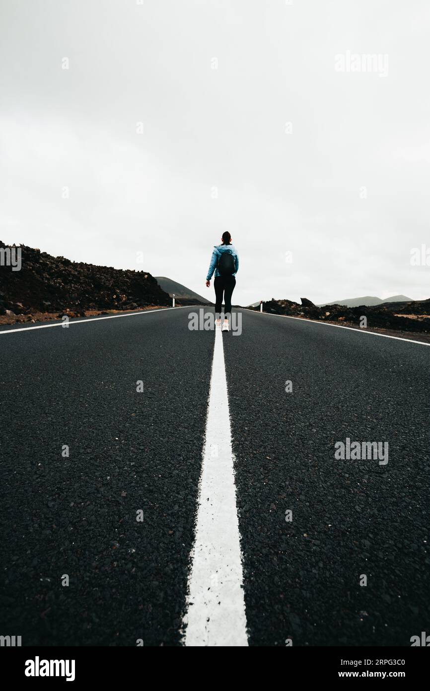 Immagine verticale di una strada vuota con una donna turistica (backpacker) e linee simmetriche perfette durante il giorno coperto. Viaggio scattato dal viaggio dell'isola di Lava - Lanz Foto Stock