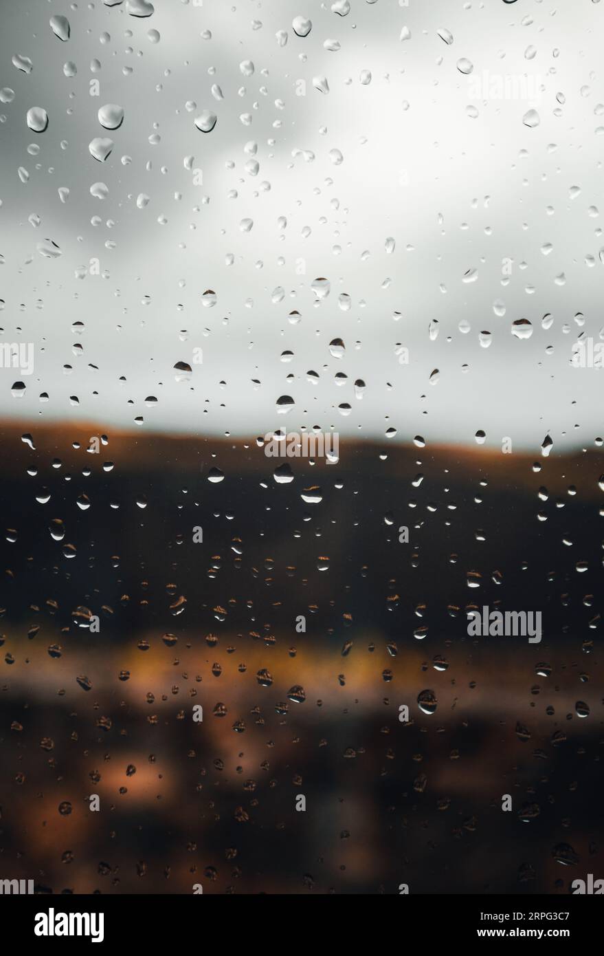 Immagine ravvicinata di gocce di pioggia sulla finestra con cielo nuvoloso sullo sfondo. Immagine verticale di gocce di pioggia sul vetro con esterno sullo sfondo in caso di pioggia Foto Stock