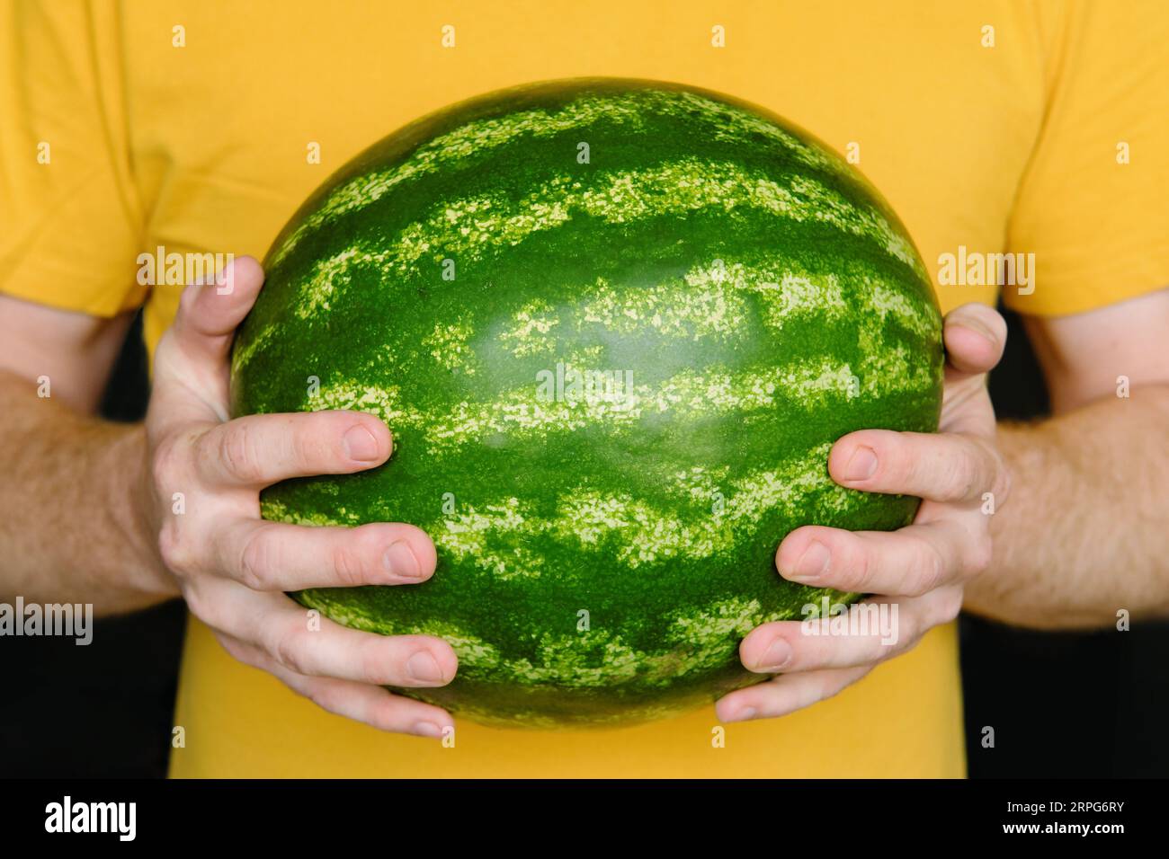 L'uomo tiene in mano l'anguria matura. Il tizio con la maglietta gialla tiene l'anguria. Foto Stock