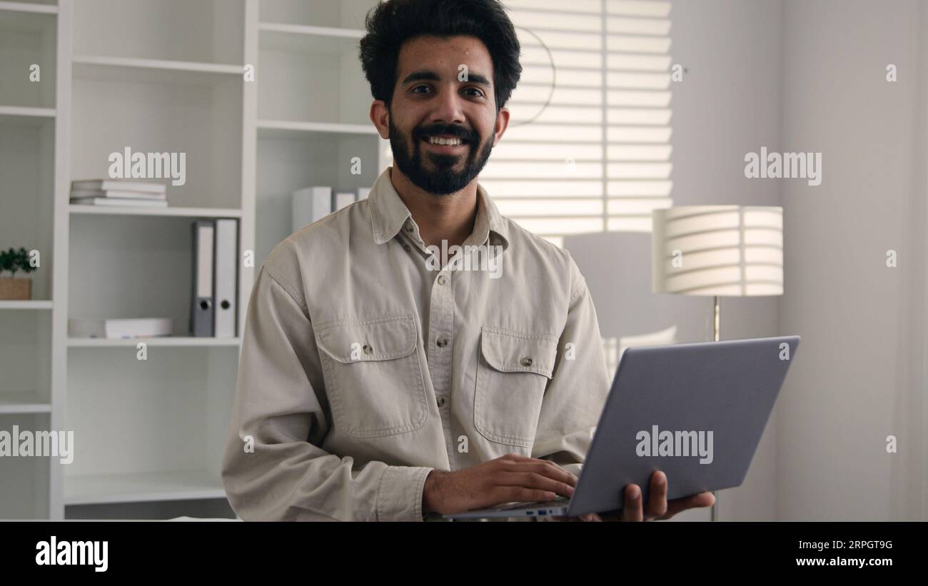Uomo d'affari indiano musulmano che lavora da casa ufficio lavoro remoto sorridendo arabo barbuto ragazzo 30s freelancer stand con laptop digitazione progetto aziendale Foto Stock