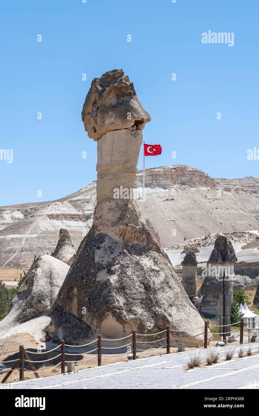 Un grande camino delle fate nel museo all'aperto di Göreme in Cappadocia, Anatolia Turchia, con una bandiera turca che sventola al vento, verticale Foto Stock