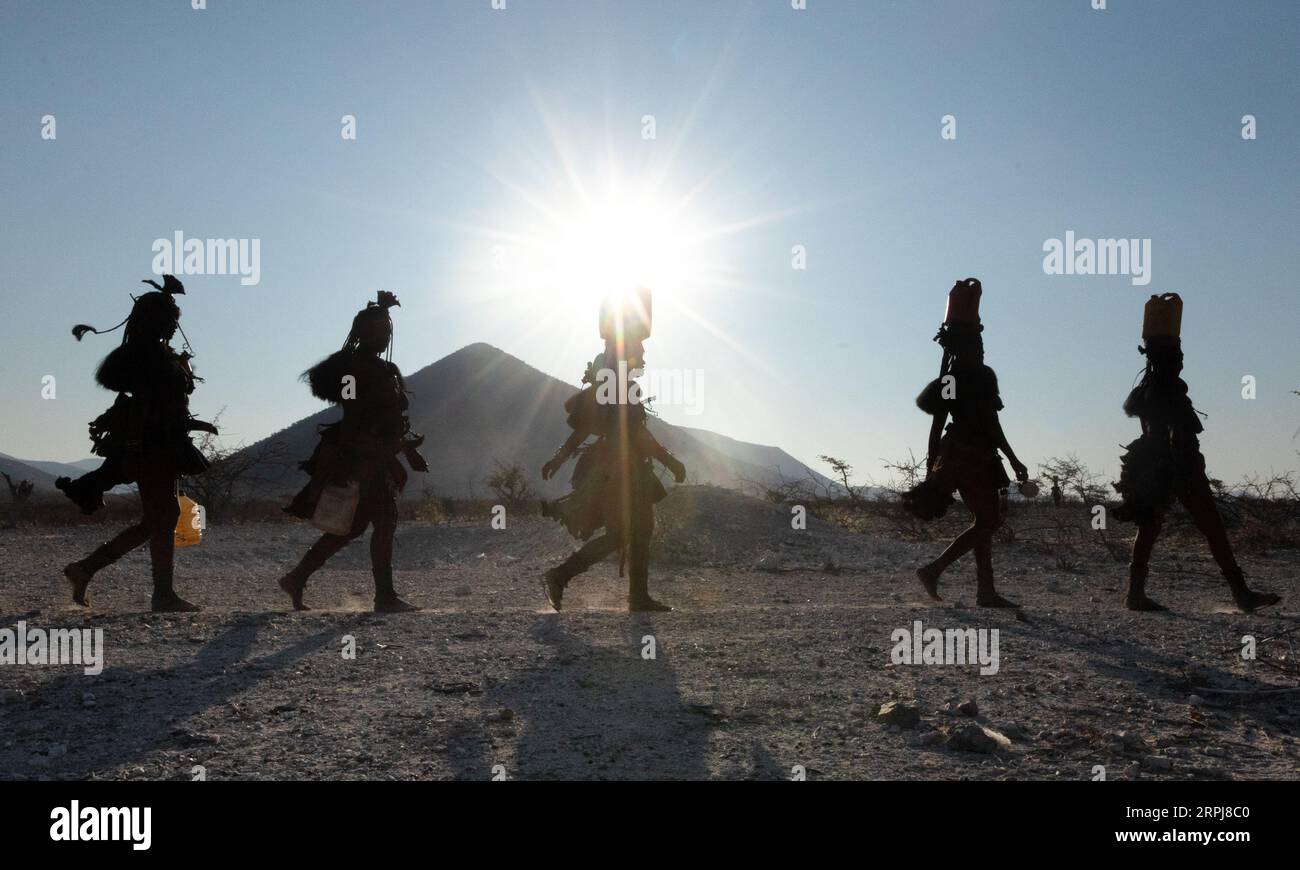 Le donne Himba camminano tutte in una sola fila mentre tornano dalla raccolta dell'acqua. L'acqua è spaventosa nella Namibia settentrionale, quindi tutte le razioni devono essere raccolte su Foto Stock