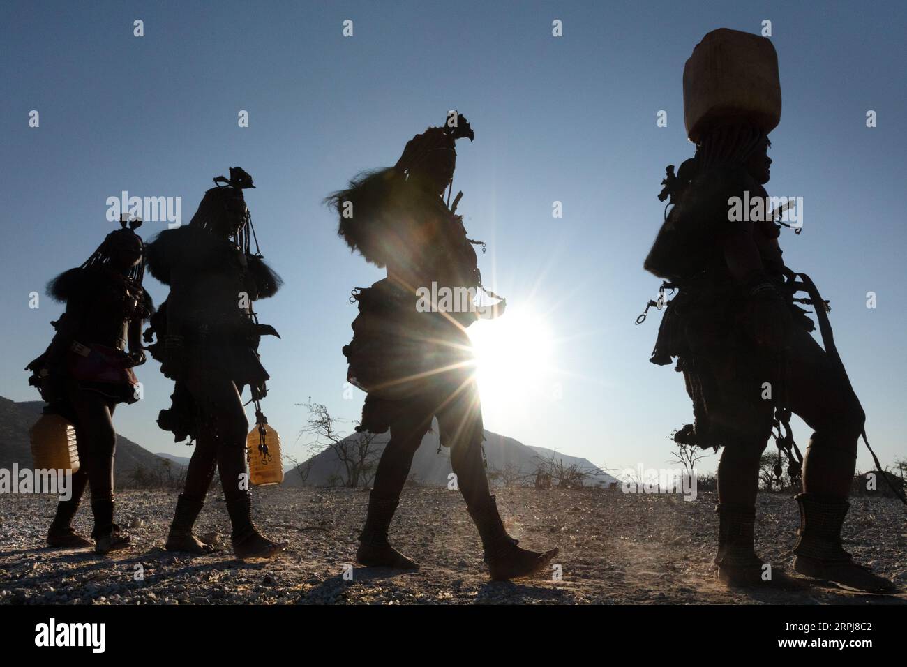 Le donne Himba camminano tutte in una sola fila mentre tornano dalla raccolta dell'acqua. L'acqua è spaventosa nella Namibia settentrionale, quindi tutte le razioni devono essere raccolte su Foto Stock