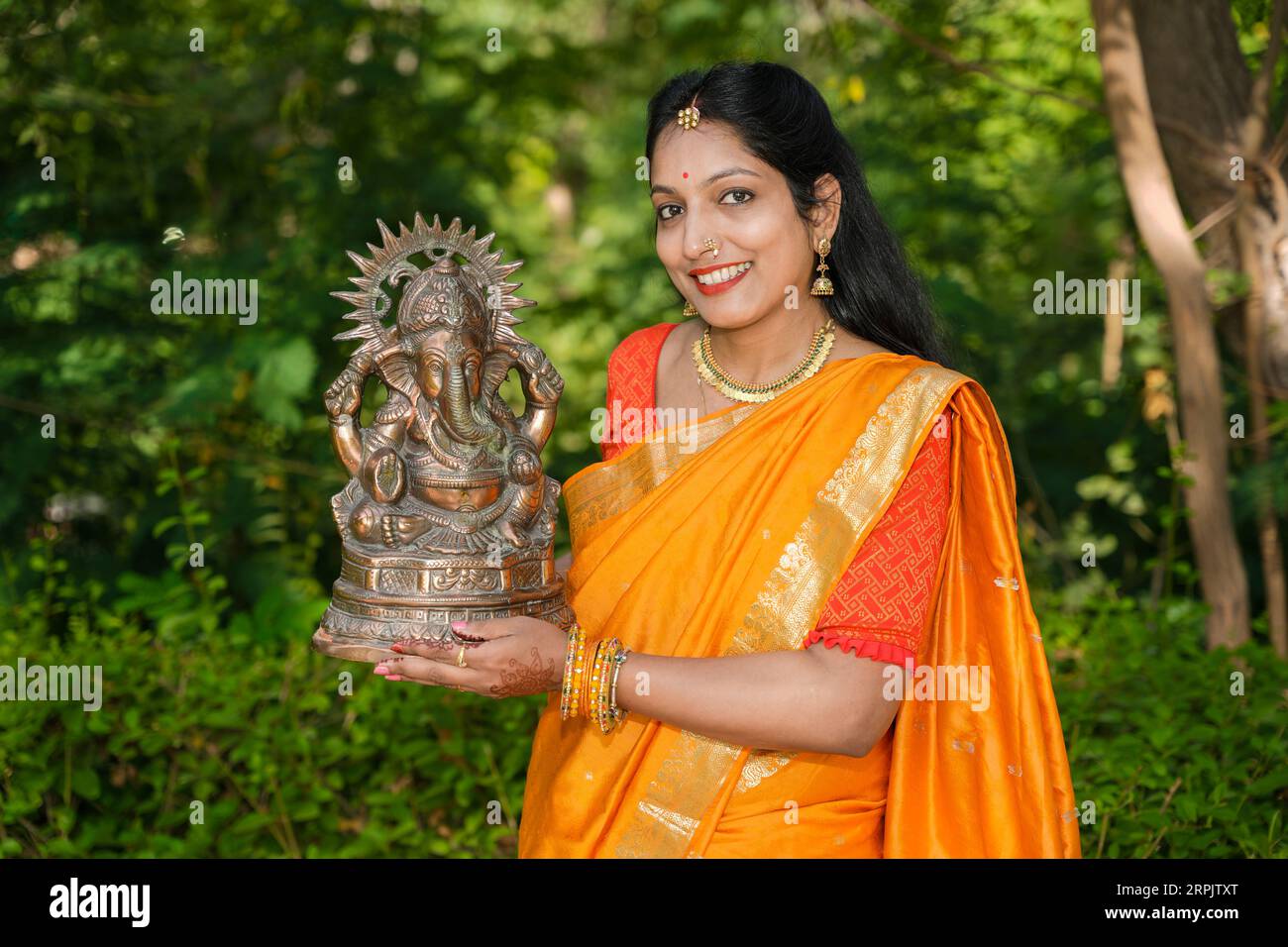 Giovane donna indiana felice che indossa sari che tiene l'idolo del signore Ganesha all'aperto nel parco che celebra il festival Ganesh Chaturthi. Foto Stock