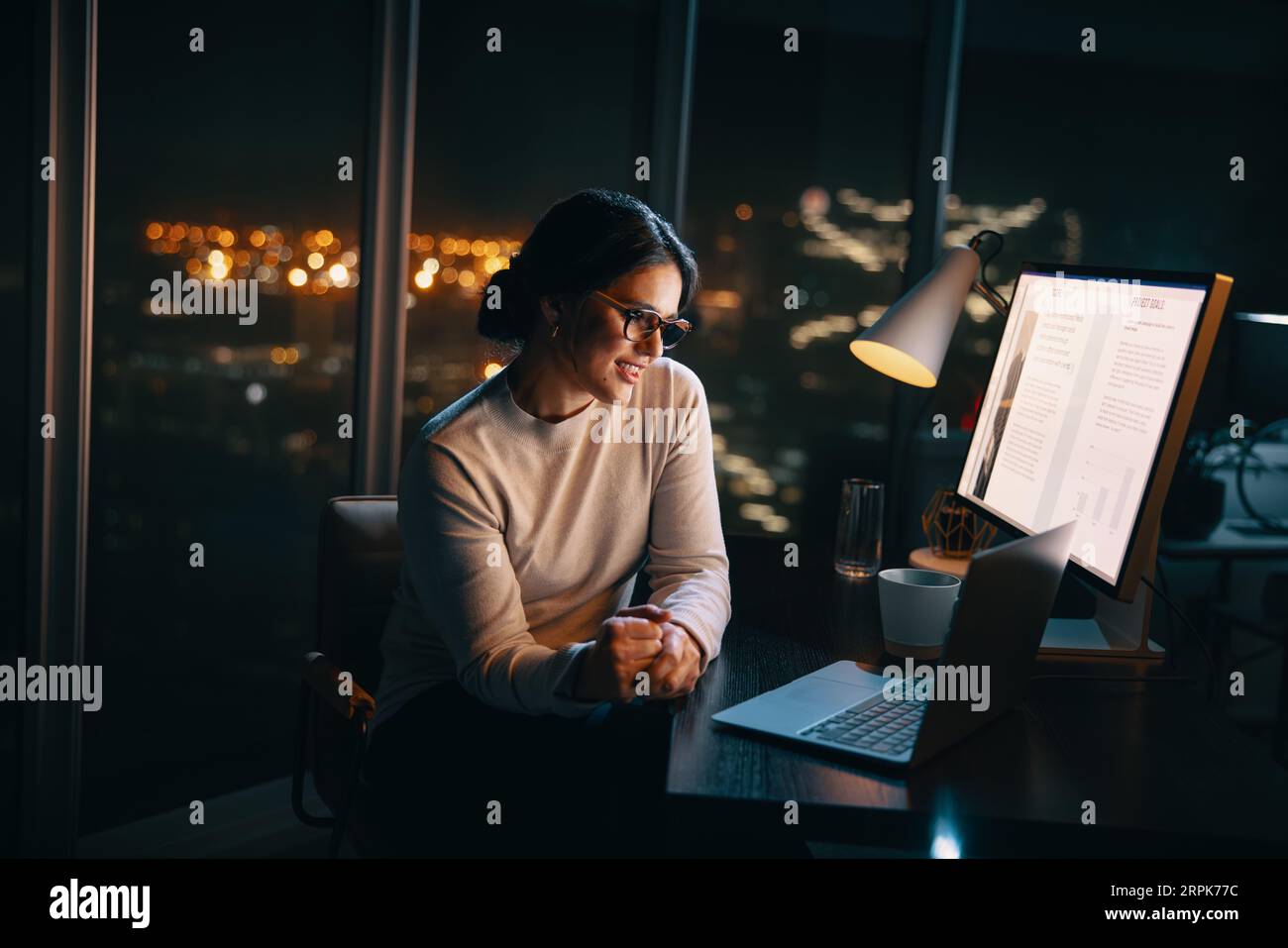 donna d'affari che partecipa a una riunione d'ufficio a tarda notte, utilizza il laptop per una videochiamata. Discute un progetto con i colleghi, mostrando dedizione Foto Stock