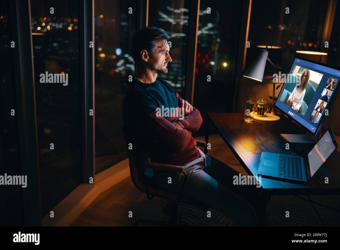 Uomo d'affari seduto alla sua scrivania in un ufficio, impegnato in una riunione notturna online con i suoi colleghi, uomo professionista che si occupa di lunghe ore Foto Stock
