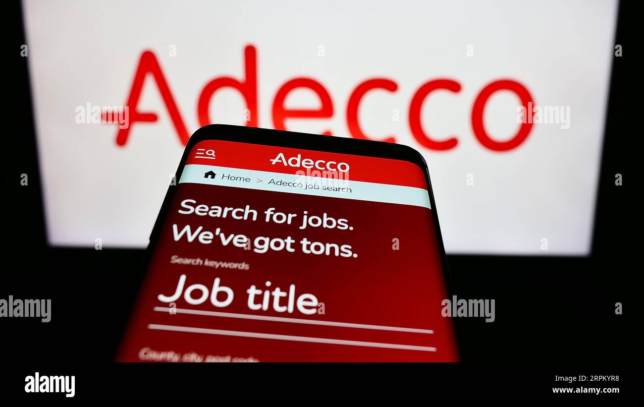 Smartphone con sito Web della società di reclutamento Adecco sullo schermo davanti al logo aziendale. Mettere a fuoco in alto a sinistra sul display del telefono. Foto Stock