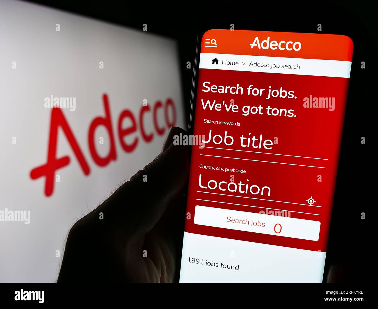 Persona in possesso di cellulare con pagina Web della società di reclutamento Adecco sullo schermo davanti al logo aziendale. Concentrarsi sul centro del display del telefono. Foto Stock