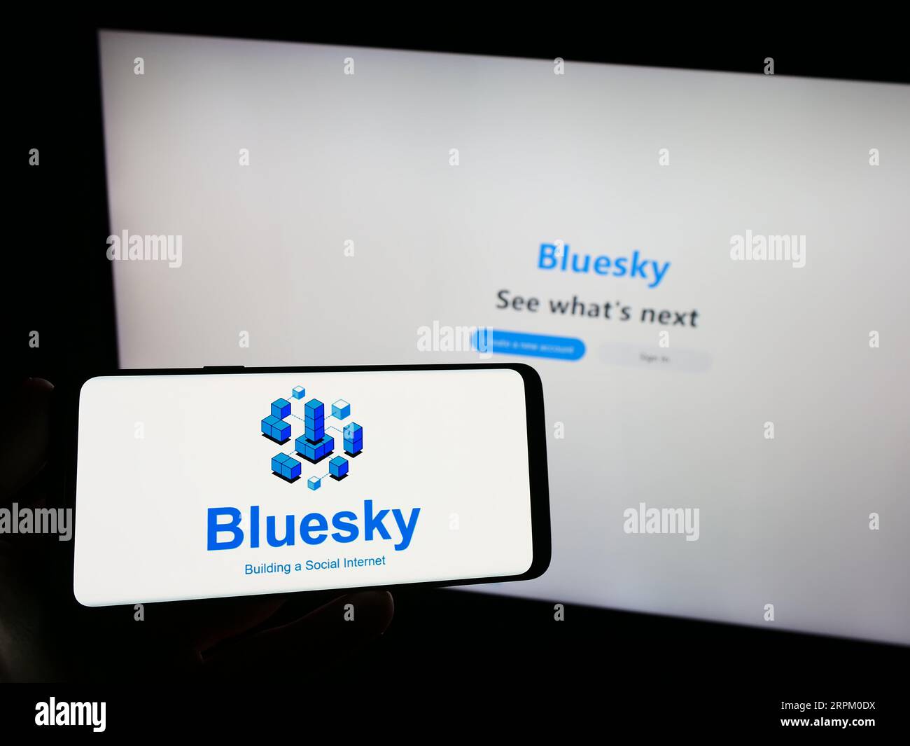 Persona che possiede uno smartphone con il logo dell'iniziativa di social network Bluesky sullo schermo di fronte al sito Web. Concentrarsi sul display del telefono. Foto Stock