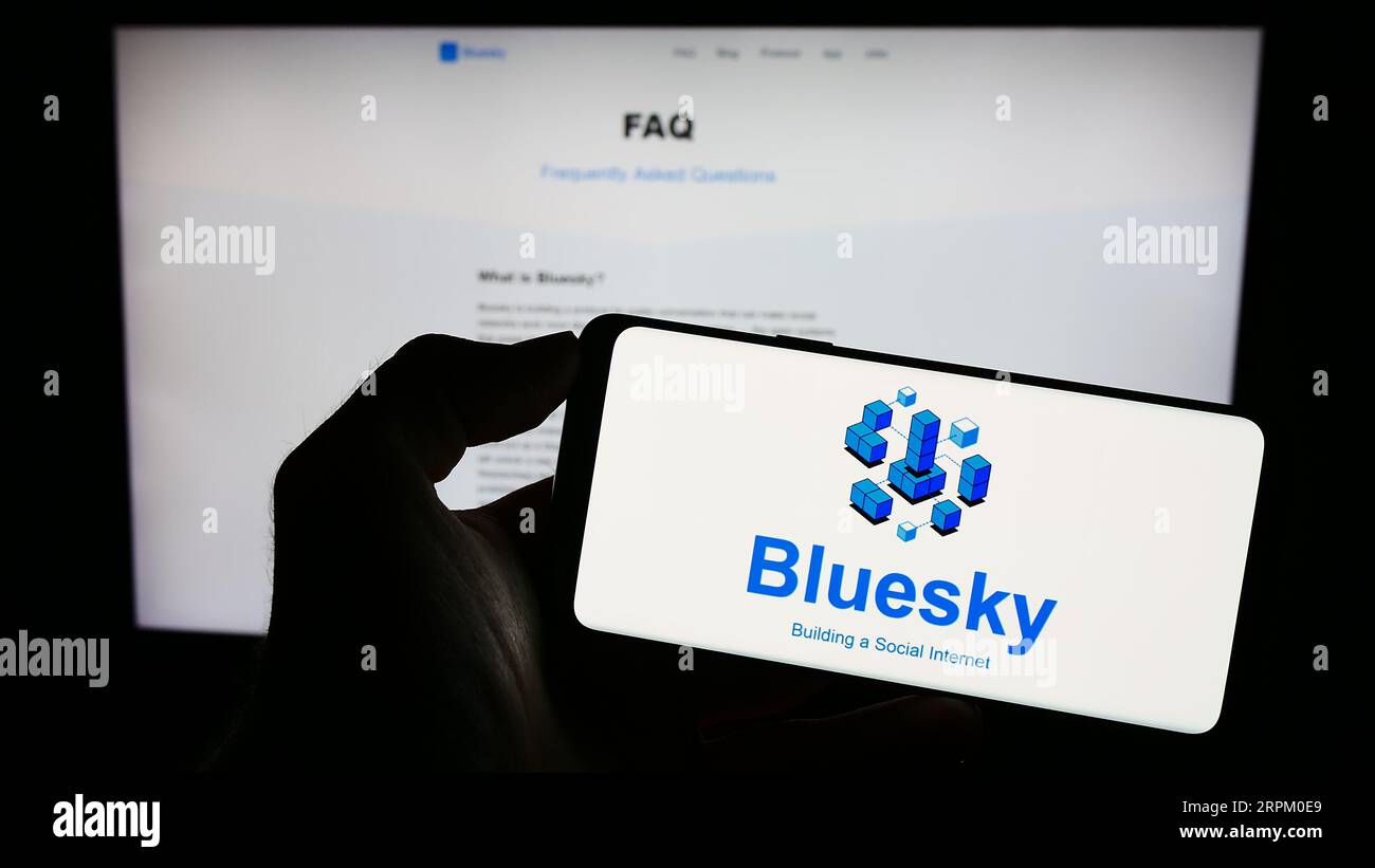 Persona che possiede il cellulare con il logo dell'iniziativa di social network Bluesky sullo schermo di fronte alla pagina Web. Concentrarsi sul display del telefono. Foto Stock