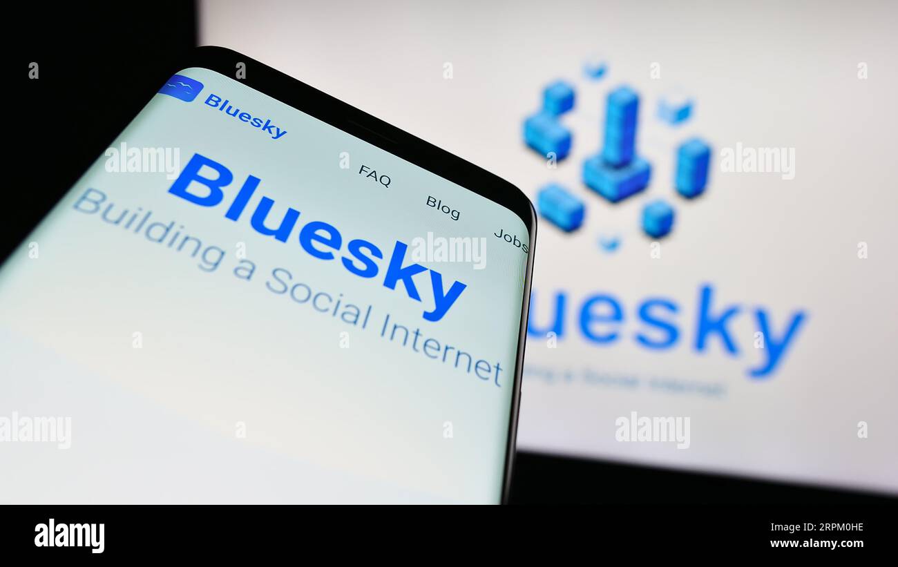 Telefono cellulare con sito Web dell'iniziativa di social network Bluesky sullo schermo davanti al logo. Mettere a fuoco in alto a sinistra sul display del telefono. Foto Stock