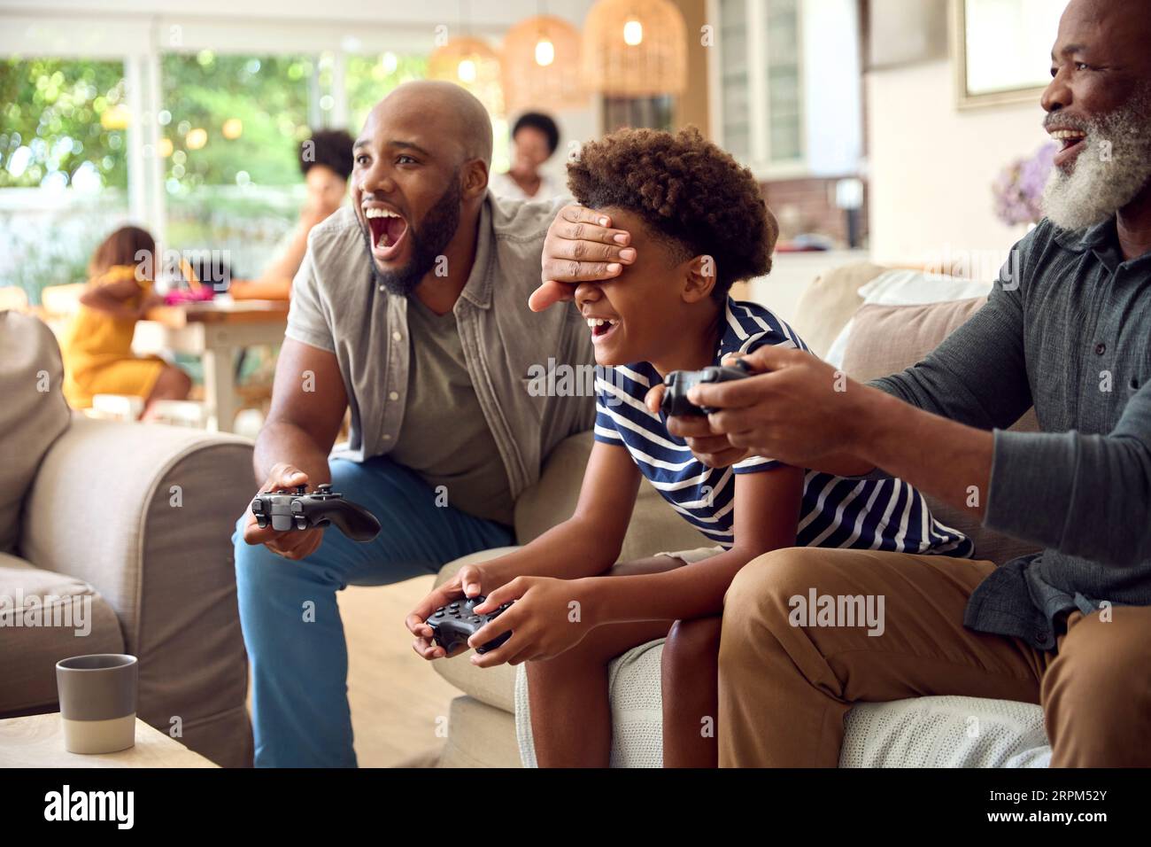 Famiglia maschile di più generazioni seduto sul divano a casa a giocare a un videogioco con papà che tradisce Foto Stock