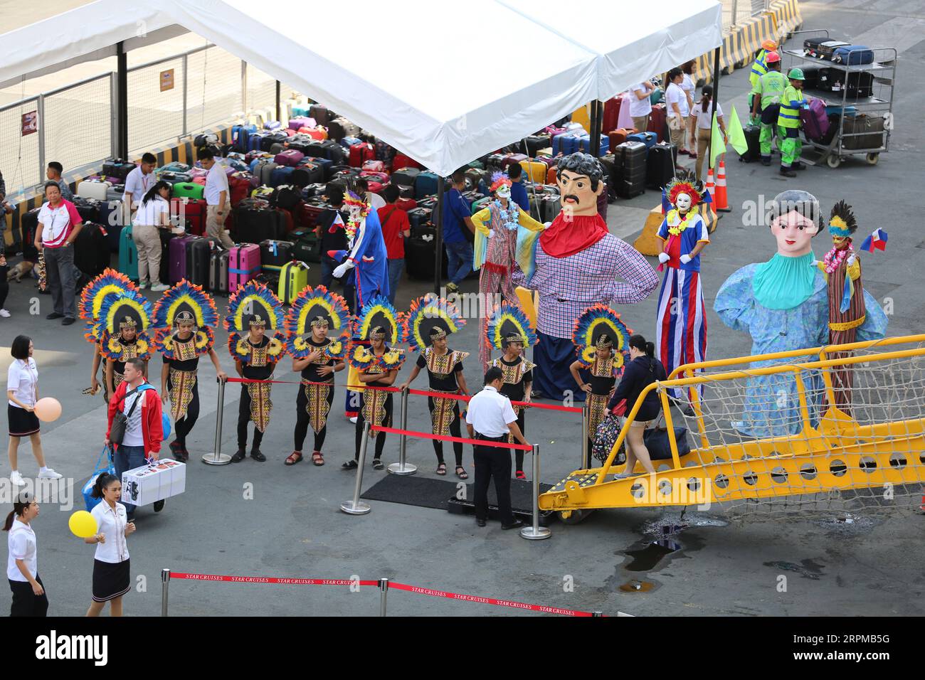Festa di benvenuto a tema festa filippina per la nave da crociera al molo di Manila: Musicisti con strumenti di bambù, ballerini filippini, Higantes, bandiere Foto Stock