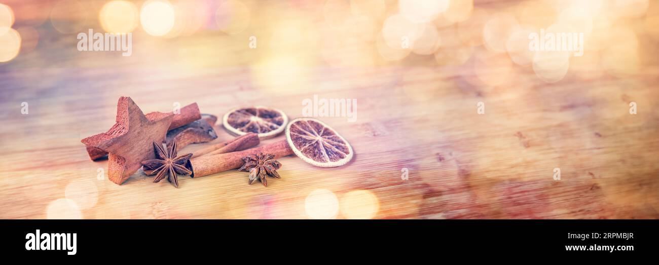 Spezie con arancia secca e cannella su fondo di legno con luci sfocate, banner web panoramico natalizio Foto Stock