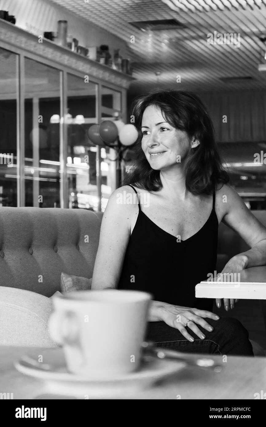 Bella donna che beve caffè al bar, monocromatico. Vita quotidiana, in bianco e nero. Godetevi la vostra vita. Bruna con una tazza di tè sul divano. Foto Stock